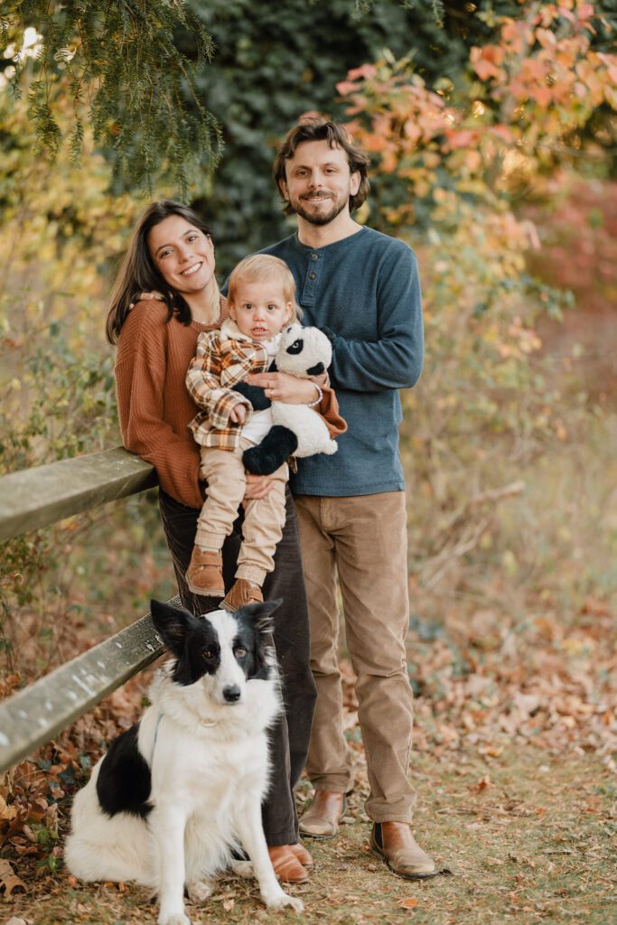 Fall photo of family and dog next to rustic fence